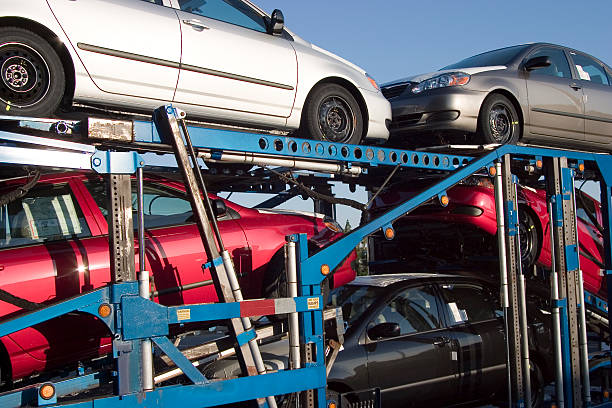 Several cars are stacked on a blue car carrier trailer, with two on the top level and three below, ready for OR Auto Transport Portland under a clear sky.